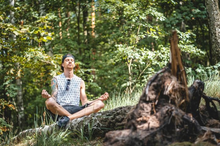 Arrêter le cannabis : un homme assis en tailleur sur un tronc d’arbre, les yeux fermés, méditant dans une forêt Arrêter le cannabis : un homme assis en tailleur sur un tronc d’arbre, les yeux fermés, méditant dans une forêt